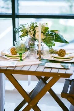 Table decorated with plates, pineapples, candles and flowers, green and white Fotos Stock