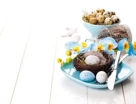 Table decoration with easter eggs nest on plate, on white wooden background Stock Photos