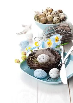 Table decoration with easter eggs nest on plate, on white wooden background Stock Photos