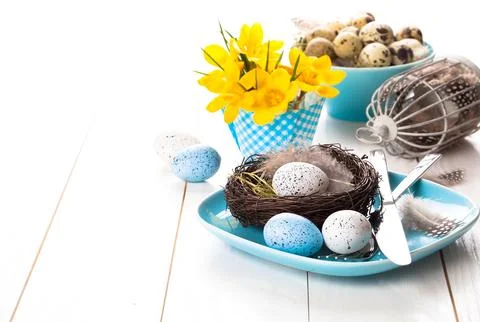 Table decoration with easter eggs nest on plate, on white wooden background Stock Photos