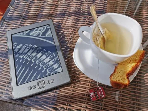Table with electronic book and tea with a sweet on a terrace to relax Stock Photos