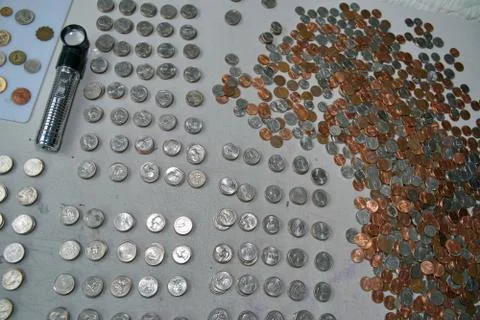 A table full of coins and a lighted loupe is a collectors environment. Stock Photos