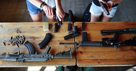 Table full of firearms arsenal cute girl reloading gun Stock Footage 58599206