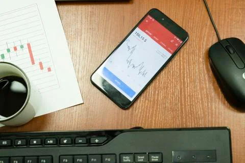 Table with keyboard, mouse, cup of coffee, market charts and smartphone. Stock Photos