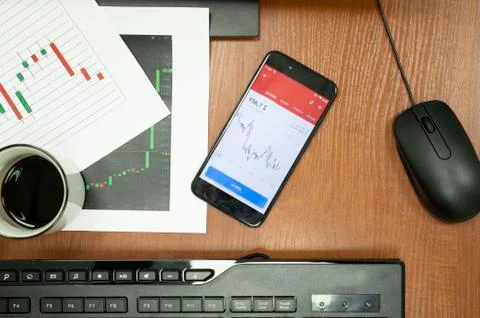 Table with keyboard, mouse, cup of coffee, market charts and smartphone. Stock Photos
