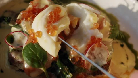 A table knife cuts a poached egg with red caviar on a lush benedict toast 스톡 동영상 151296485