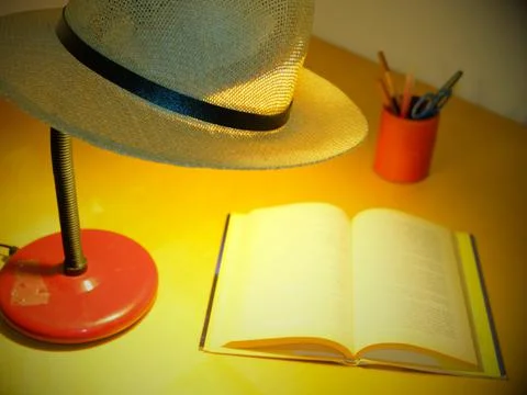 Table lamp with a Panama hat resting on top illuminates a book Stock Photos