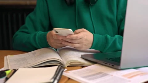 Table with laptop study materials student typing messages chatting in phone Stock Footage 274605811