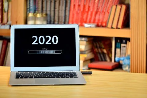 On the table laptop with text - 2020 loading - on screen, blurred shelf with  Stock Photos