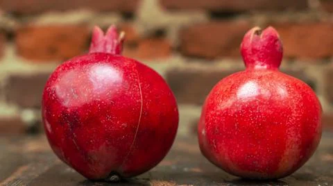 On the table lay two red pomegranate. Two ripe garnet on the table on red bri 库存照片