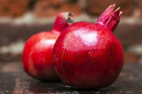 On the table lay two red pomegranate. Two ripe garnet on the table on red bri 库存照片