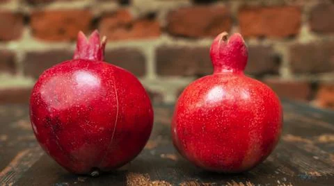 On the table lay two red pomegranate. Two ripe garnet on the table on red bri 库存照片