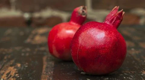 On the table lay two red pomegranate. Two ripe garnet on the table on red bri 库存照片