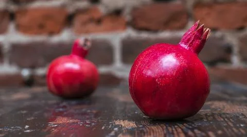 On the table lay two red pomegranate. Two ripe garnet on the table on red bri 库存照片