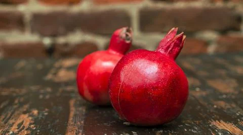 On the table lay two red pomegranate. Two ripe garnet on the table on red bri Foto stock