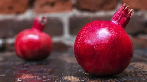 On the table lay two red pomegranate. Two ripe garnet on the table on red bri 库存照片