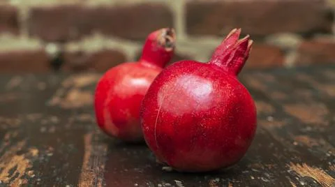 On the table lay two red pomegranate. Two ripe garnet on the table on red bri 库存照片
