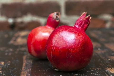 On the table lay two red pomegranate. Two ripe garnet on the table on red bri 库存照片