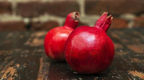 On the table lay two red pomegranate. Two ripe garnet on the table on red bri 库存照片