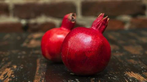 On the table lay two red pomegranate. Two ripe garnet on the table on red bri 库存照片