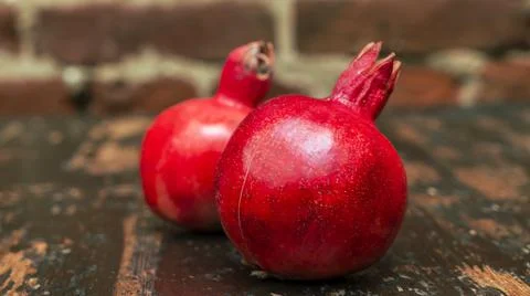 On the table lay two red pomegranate. Two ripe garnet on the table on red bri Foto stock