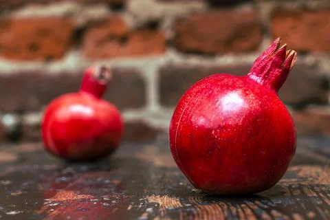 On the table lay two red pomegranate. Two ripe garnet on the table on red bri 库存照片