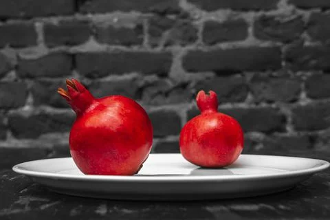 On the table lay two red pomegranate. Two ripe garnet on the table on black a 库存照片