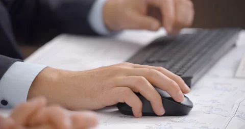 At a table, a man works at a computer and moves a black mouse  Stock Footage 161969659