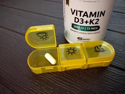 On the table is a medication organizer with vitamin D capsule in front and .. Stock Photos