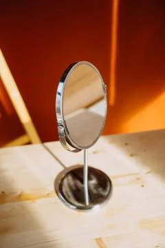Table mirror on a background of an orange wall with sunbeams. Stock Photos