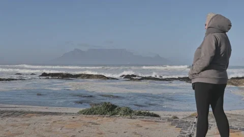 Table Mountain view from Blouberg Beach with waves crashing on rocks on a clear Stock Footage 293293596