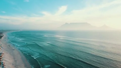 Table Mountain viewed from the coast, hazy ocean waves rolling onto a sandy.. Stock Footage 302308287