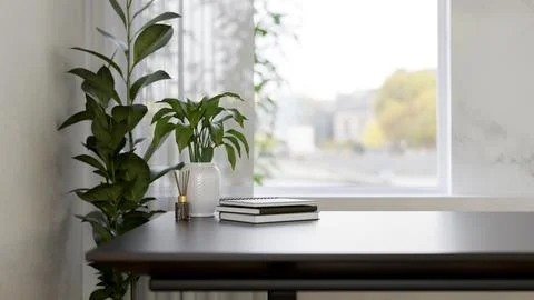 A table near the window featuring a reed diffuser, books, and plants in a m.. Stock Photos
