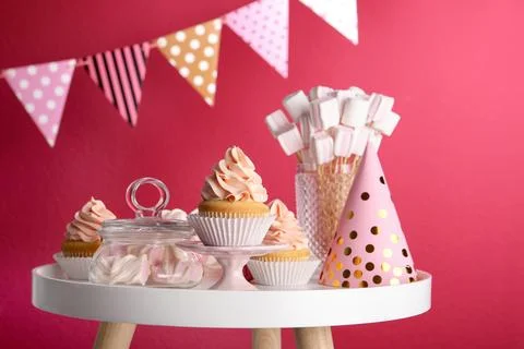 Table with party hat, cupcake and other sweets on burgundy background. Candy  Stock Photos