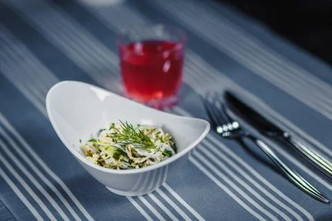Table in the restaurant. On the table is a salad in a white plate, a knife, a Stock Photos