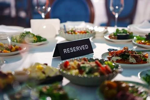 Table set for dinner with reserved sign and various dishes in restaurant Stock Photos