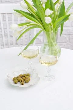 Table set with two glasses of white wine, vase with white tulips, plate with Stock Photos