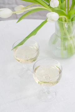 Table set with two glasses of white wine, vase with white tulips, on white table Stock Photos
