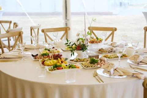 Table set with white tablecloth, plates of food, glasses, cutlery, floral Stockfoto's