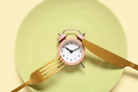 Table setting with alarm clock on beige background. Intermittent fasting conc Stock Photos