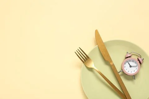 Table setting with alarm clock on beige background. Intermittent fasting conc Stock Photos