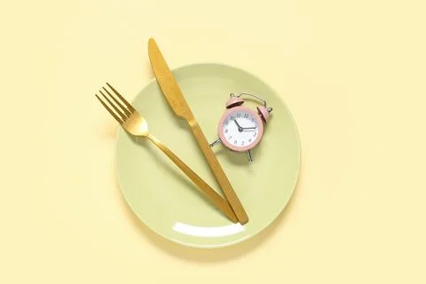 Table setting with alarm clock on beige background. Intermittent fasting conc Stock Photos