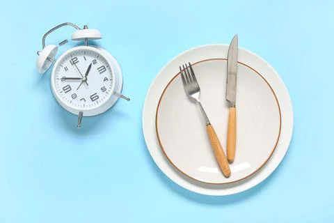 Table setting with alarm clock on blue background. Intermittent fasting conce Stock Photos