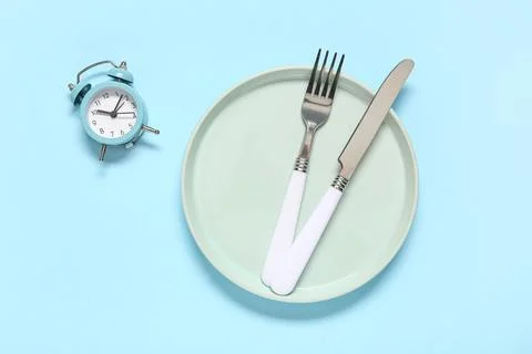 Table setting with alarm clock on blue background. Intermittent fasting conce Stock Photos