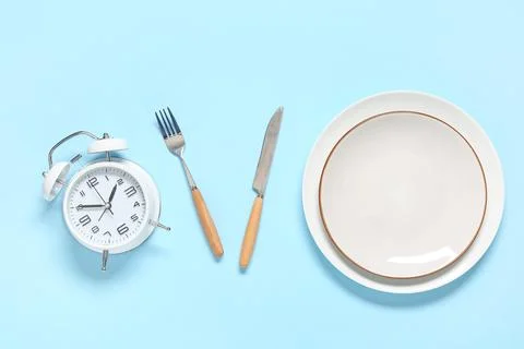 Table setting with alarm clock on blue background. Intermittent fasting conce Stock Photos