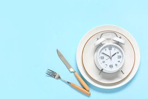 Table setting with alarm clock on blue background. Intermittent fasting conce Stock Photos