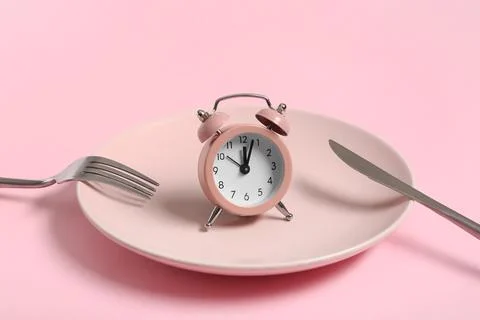 Table setting with alarm clock on pink background. Intermittent fasting conce Stock Photos