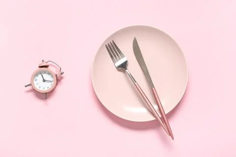 Table setting with alarm clock on pink background. Intermittent fasting conce Stock Photos