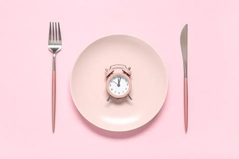 Table setting with alarm clock on pink background. Intermittent fasting conce Stock Photos