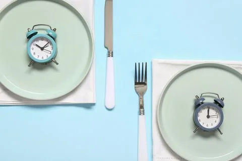 Table setting with alarm clocks on blue background. Intermittent fasting conc Stock Photos